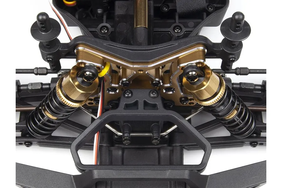 Close-up of a gold anodized aluminium front shock tower installed on an RC car chassis with black suspension components.