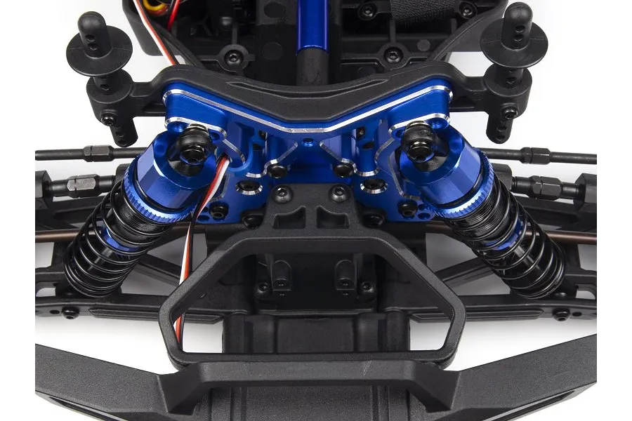 A close-up view of a blue aluminium front shock tower installed on an RC car chassis, featuring black coil-over shocks and a black plastic bumper.