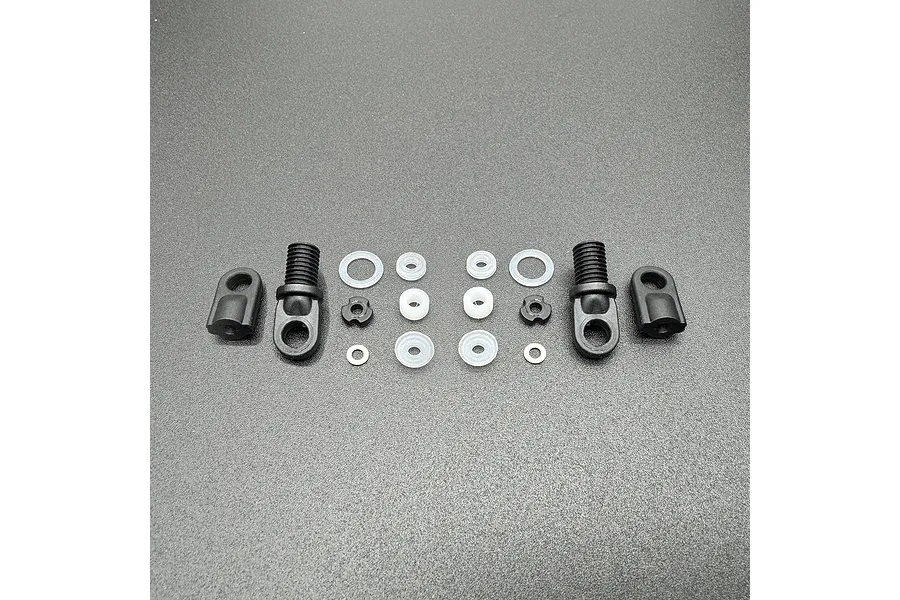 A set of RC shock rebuild components including two threaded shock caps, two rod ends, and various O-rings and spacers laid out on a grey surface.