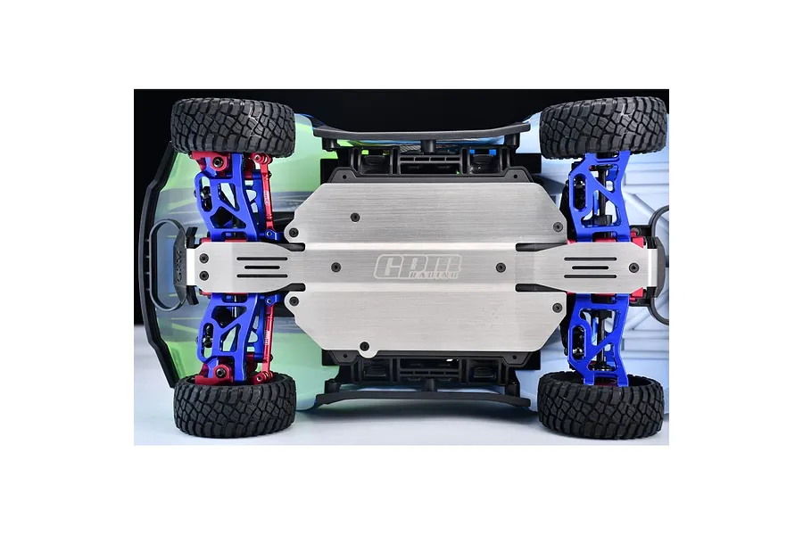 Bottom view of an RC car chassis featuring a GPM Racing stainless steel skid plate installed, with blue and red suspension components visible.
