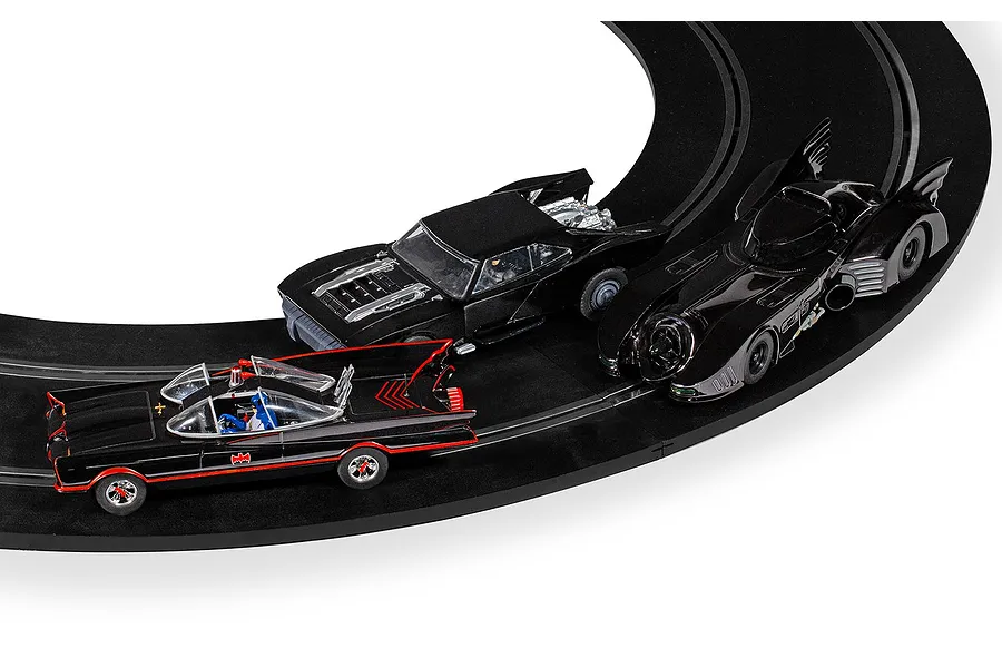 Three Scalextric Batmobile slot cars racing on a curved black track, including the 1966 classic, the 1989 movie version, and a modern muscle car style Batmobile.