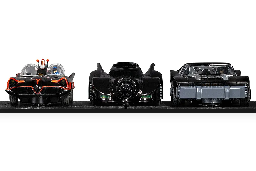 Three Scalextric Batmobile slot cars lined up on a black track, including the 1966, 1989, and The Batman versions.