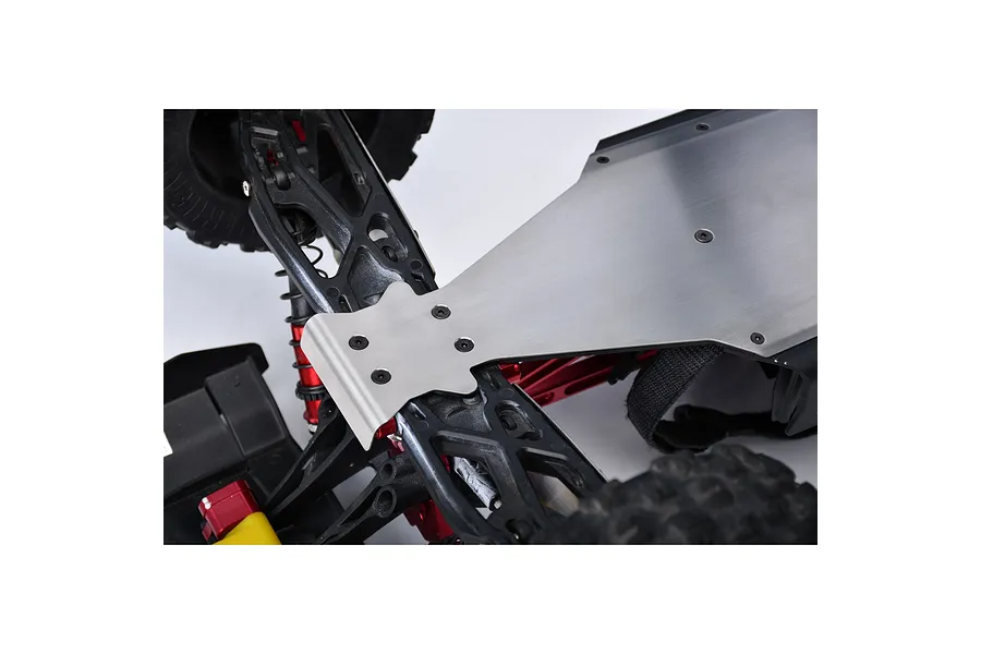 A silver stainless steel skid plate installed on the underside of an RC vehicle chassis, showing mounting screws and surrounding suspension components.