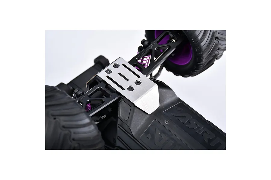 A silver GPM stainless steel skid plate installed on the front chassis of an RC monster truck with black suspension arms and purple springs.