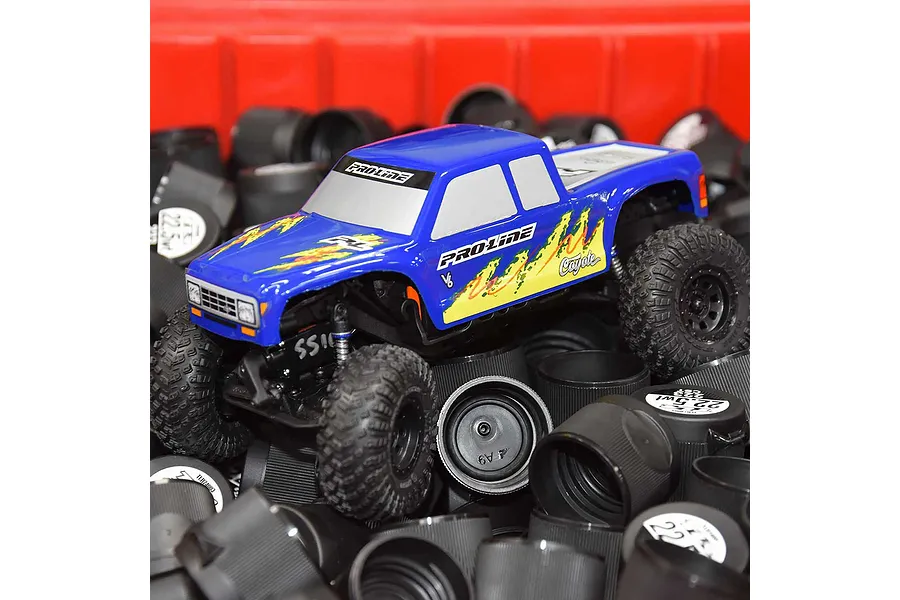 A blue Pro-Line Coyote RC truck body shell mounted on a chassis, sitting atop a pile of black plastic shock oil bottle caps.