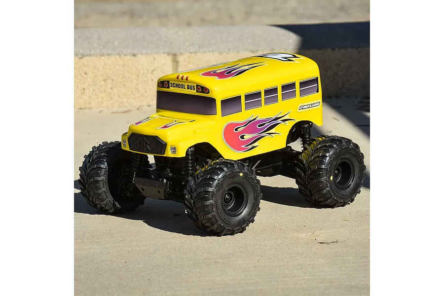 A yellow Pro-Line RC school bus body shell mounted on a monster truck chassis, featuring flame decals and black off-road tires on a concrete surface.