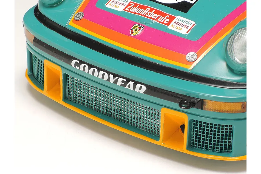 Close-up of the front bumper and hood of a Tamiya 1/24 scale Porsche 934 Turbo RSR Vaillant model car, featuring teal, orange, and pink racing livery.