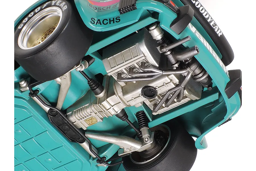 Close-up view of the detailed undercarriage and engine bay of a Tamiya 1/24 scale Porsche 934 Turbo RSR model car, showing suspension and exhaust details.