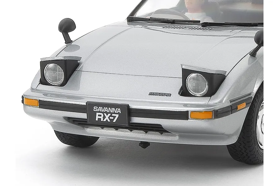 Close-up of a silver Tamiya 1/24 scale Mazda Savanna RX-7 model car showing the front bumper, pop-up headlights, and license plate.