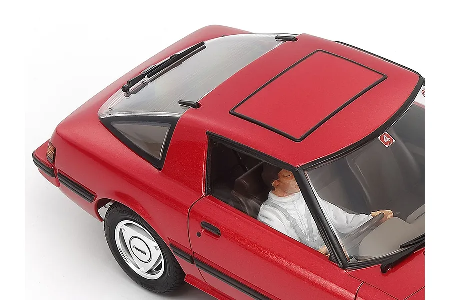 High-angle close-up of a red 1/24 scale Tamiya Mazda Savanna RX-7 model car showing the roof, rear window, and driver figure.