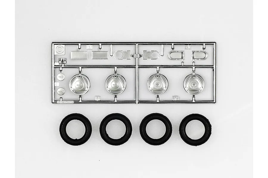 A Tamiya plastic model kit parts sprue featuring chrome-plated wheel components and four separate black rubber tires.