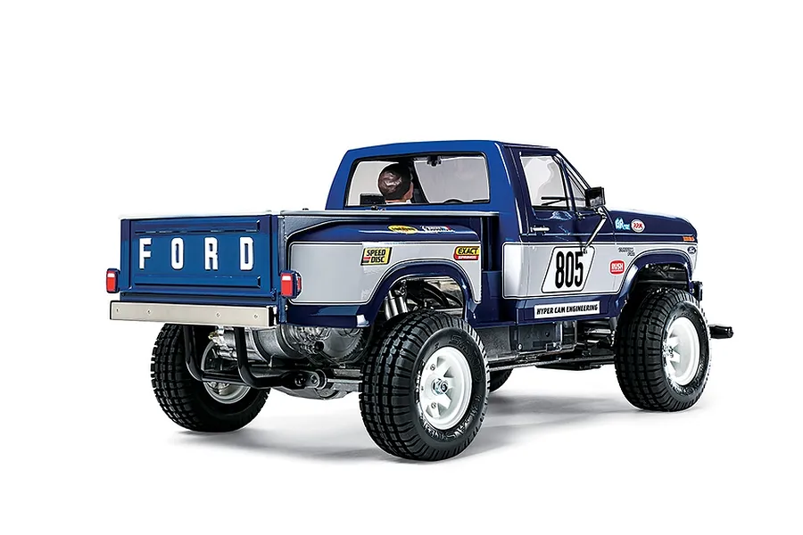 Rear three-quarter view of a Tamiya Ford F-150 Ranger XLT RC truck model with blue and silver paint, racing decals, and white wheels on a white background.