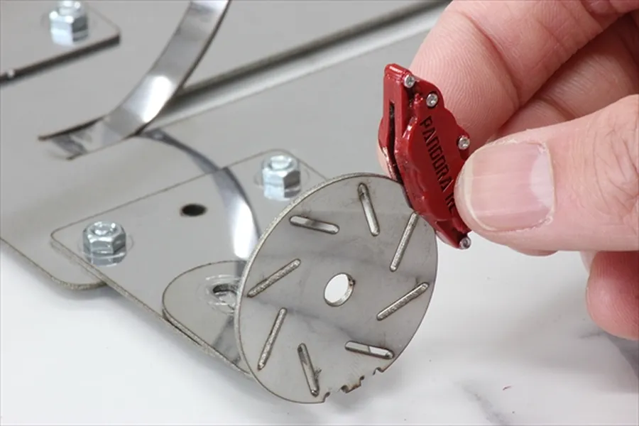 A hand holding a red Pandora RC brake caliper accessory next to a metal RC brake disc component.
