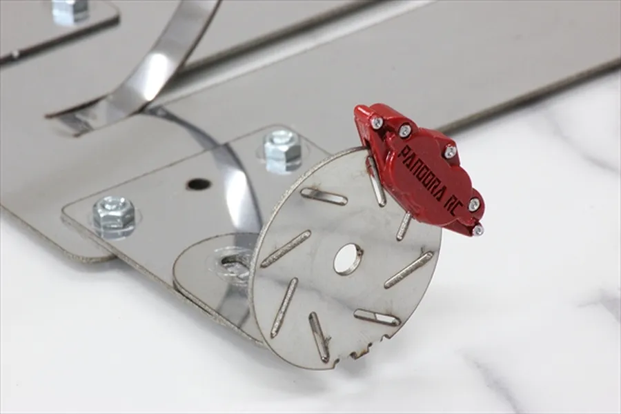 A red Pandora RC brake caliper mounted on a silver metal brake disc, attached to a larger metal mounting plate.