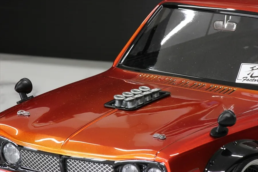Close-up of a metallic orange RC car body shell featuring silver velocity stacks mounted on the hood.