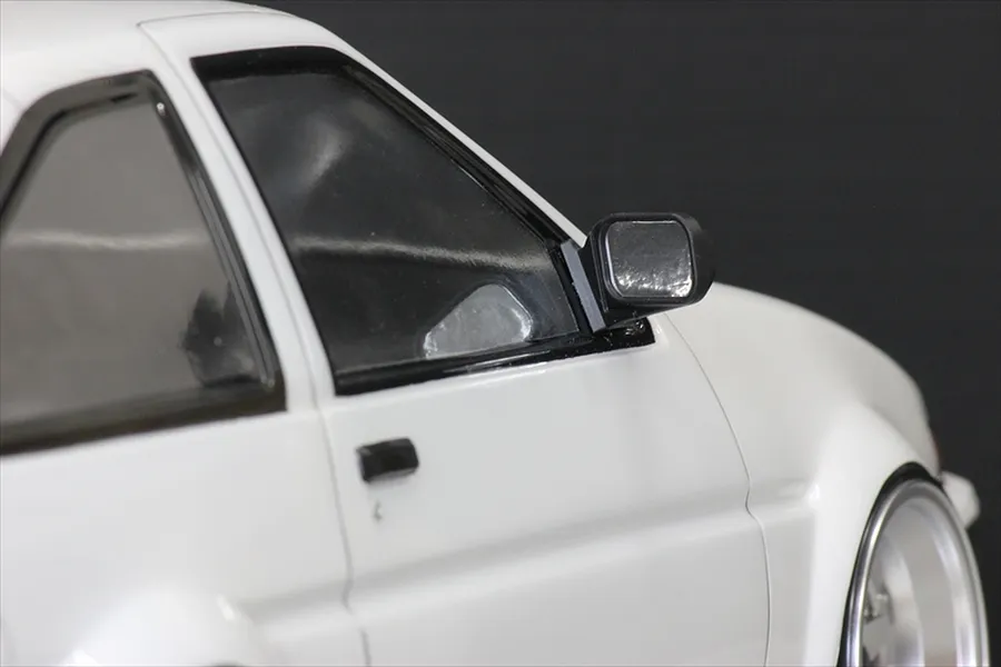 Close-up of a white 1/10 scale RC car body featuring a black side mirror mounted on the door frame.