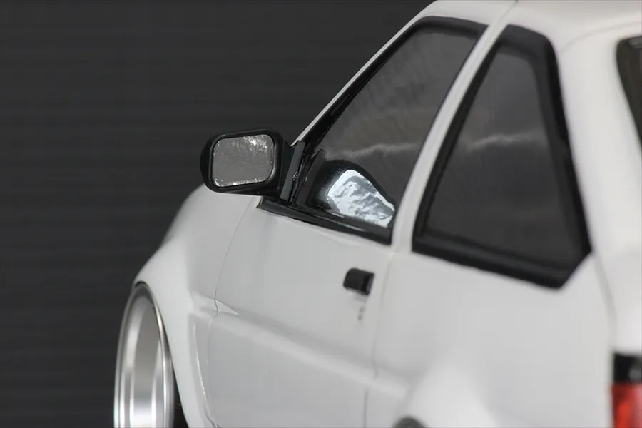 Close-up of a white 1/10 scale RC car body shell featuring a black side door mirror mounted on the driver side door.