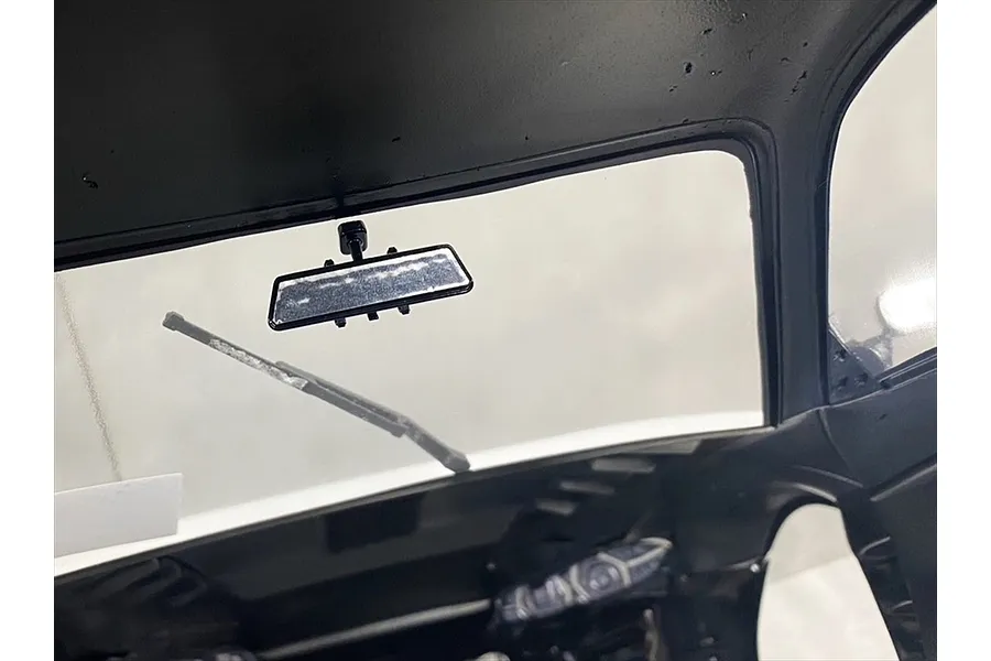 Interior view of an RC car body shell showing a small black rearview mirror mounted to the roof and a windshield wiper.