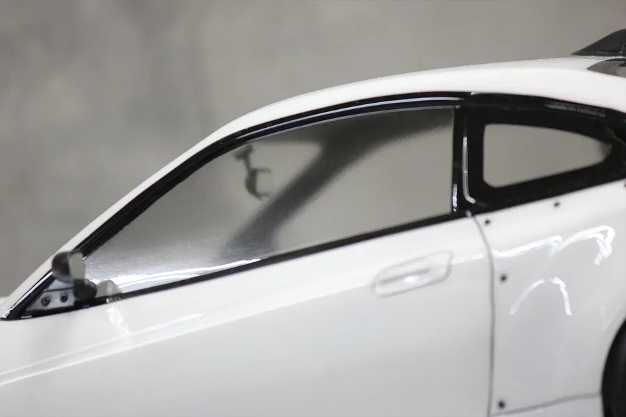 Close-up of a white RC car body shell showing the side window, door handle, and a small black side mirror attached to the door frame.