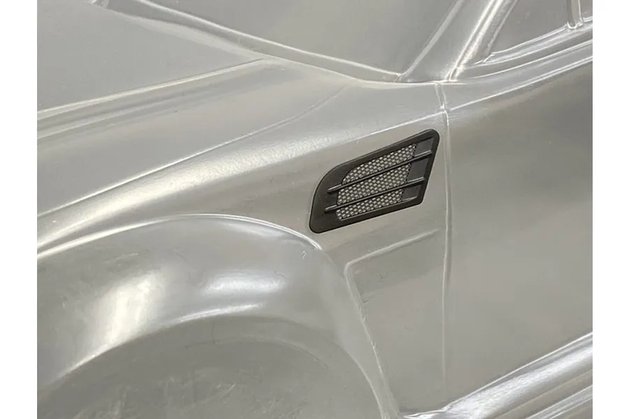 A black plastic fender duct accessory installed on a clear, unpainted 1/10 scale RC car body shell.