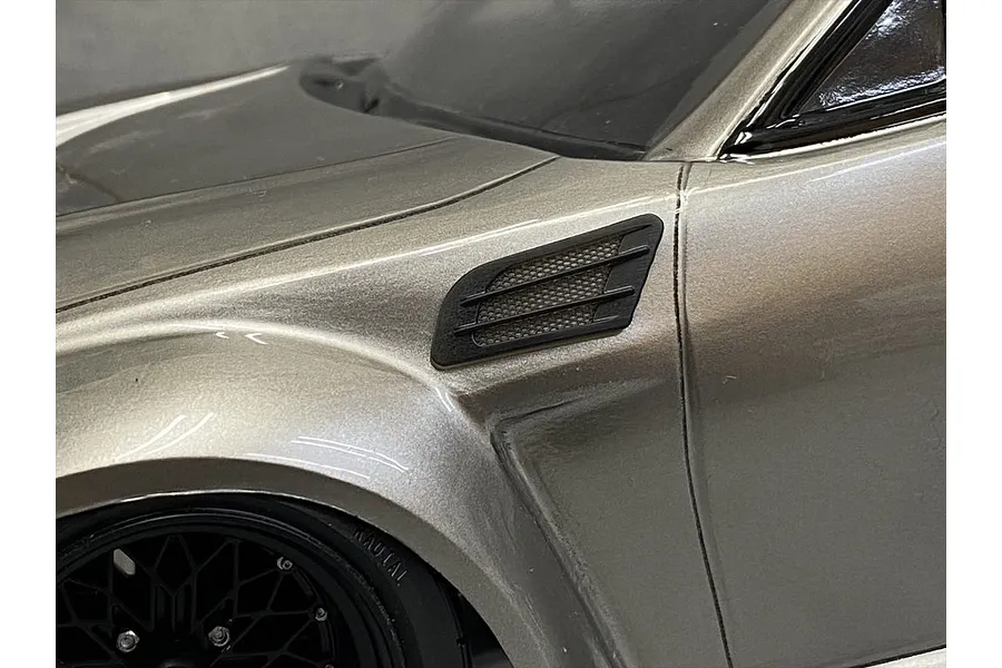 A close-up view of a black fender duct accessory installed on the side of a metallic silver RC car body shell.