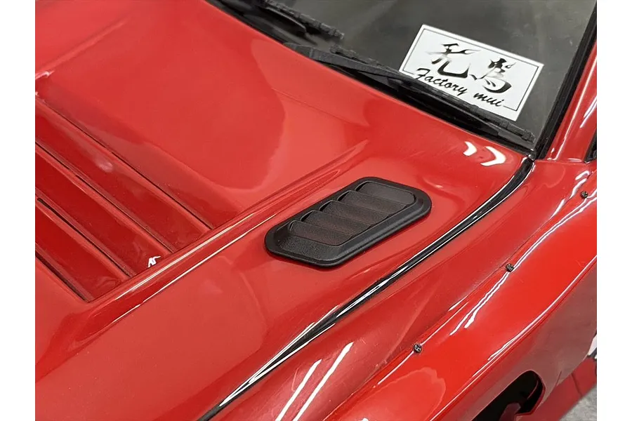 A close-up view of a black plastic bonnet duct installed on the red hood of an RC car body shell.