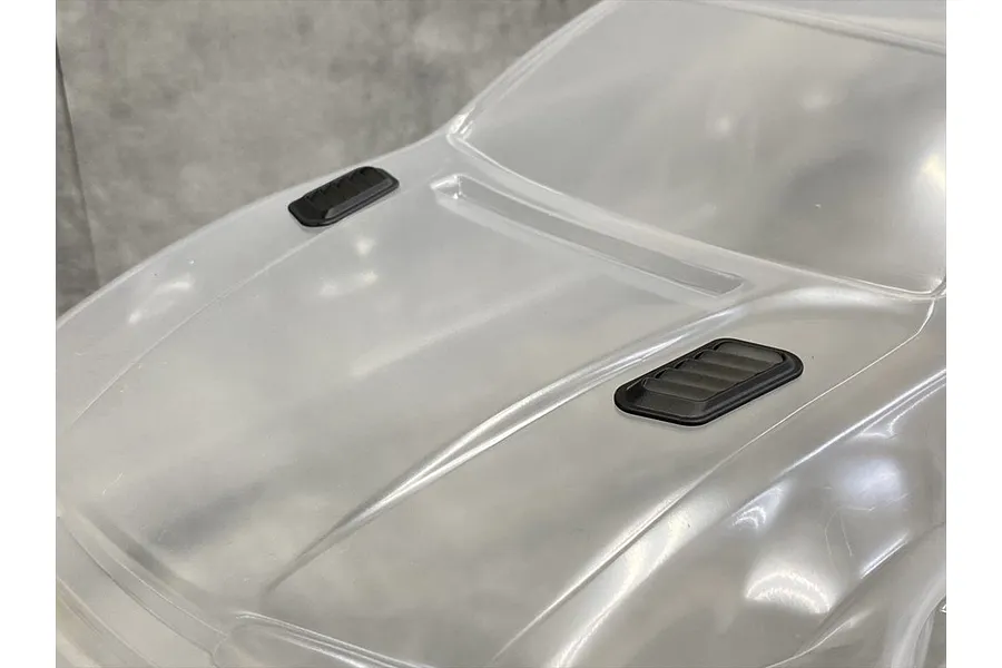 A close-up view of two black plastic bonnet ducts installed on a clear, unpainted 1/10 scale RC car body shell.