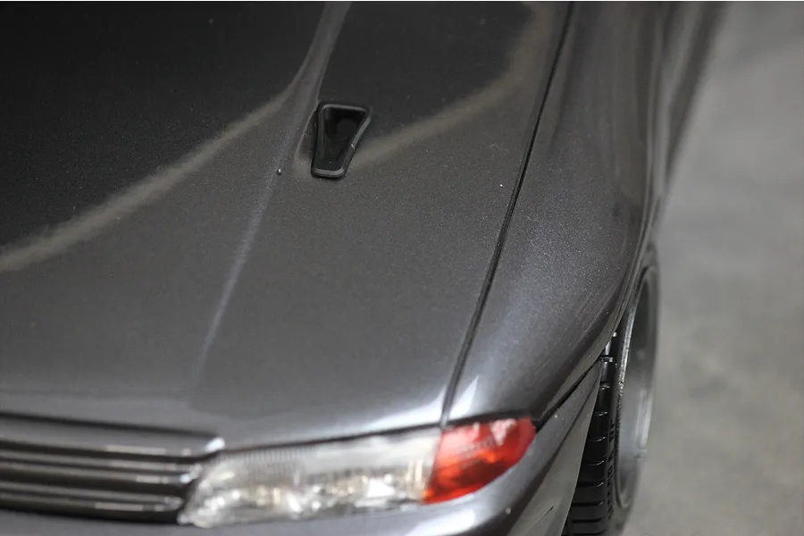 A close-up view of a dark grey RC car body shell featuring a small black NACA duct installed on the hood.