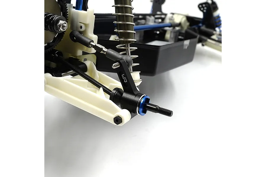 A close-up of a black aluminium RC rear hub installed on a white plastic suspension arm of an RC car chassis.