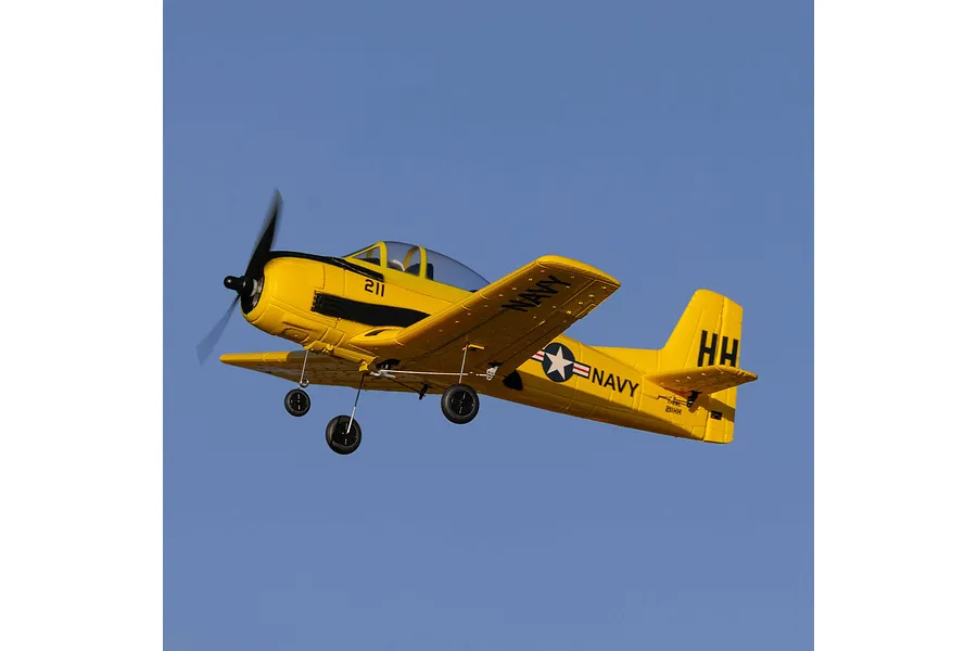 A yellow HobbyZone T-28 Trojan RC plane in flight against a clear blue sky, showing its landing gear extended.