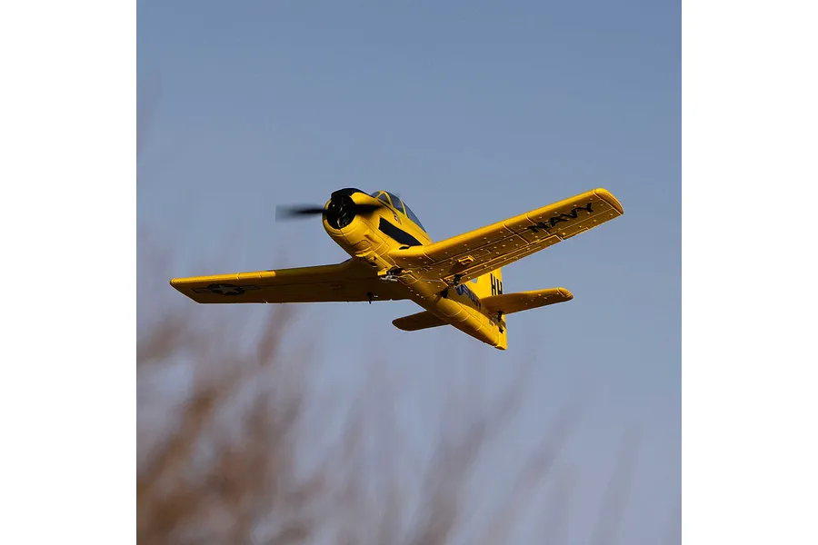 A yellow HobbyZone T-28 Trojan RC plane in flight against a clear blue sky.
