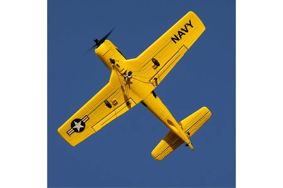 A yellow HobbyZone T-28 Trojan RC plane flying against a clear blue sky, viewed from underneath showing the landing gear and Navy markings.