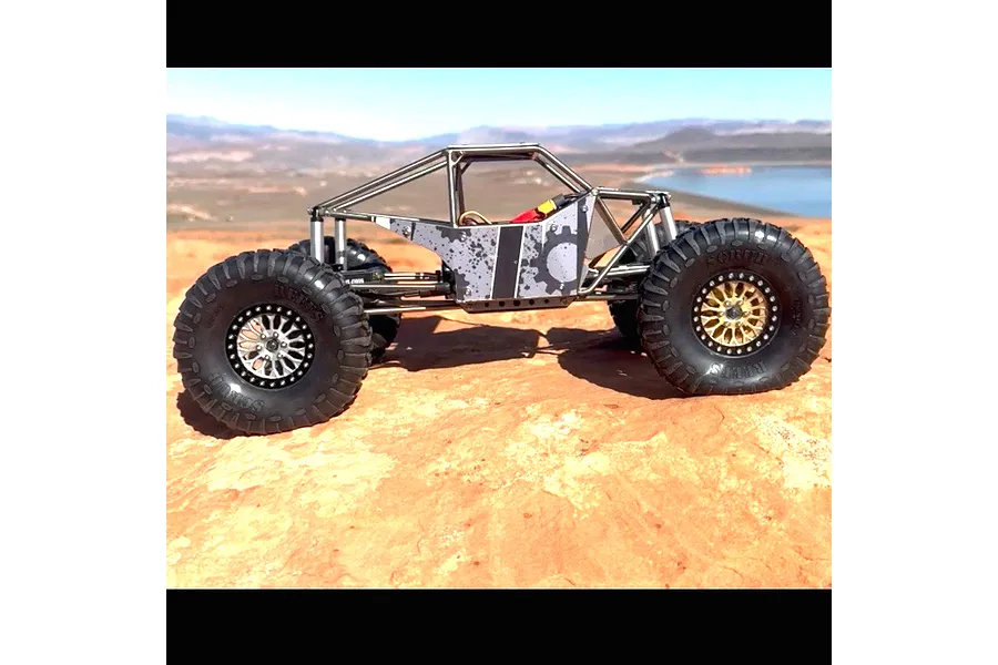 Side profile of an RC crawler vehicle equipped with Reefs RC Scrub tyres, parked on a rocky outdoor terrain.