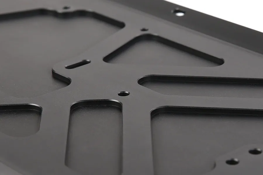 A close-up view of a black anodized aluminium RC main chassis plate with machined cutouts and mounting holes.
