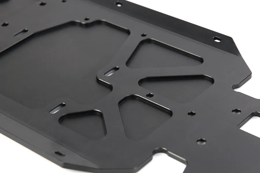 A close-up view of a black anodized aluminium RC car main chassis plate with various mounting holes and cutouts.