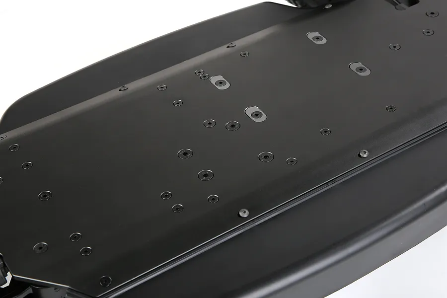 A close-up view of the underside of a black Rovan V5 aluminium RC chassis, showing the flat surface with numerous screw holes and mounting points.
