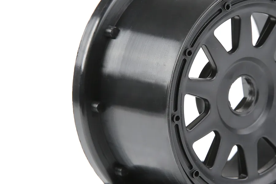 A close-up side view of a black 1/5 scale RC short course truck rear wheel rim on a white background.