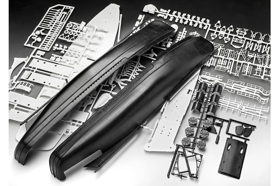 Unassembled plastic model kit parts for a ship, including large black hull sections and various white and black sprues on a white surface.