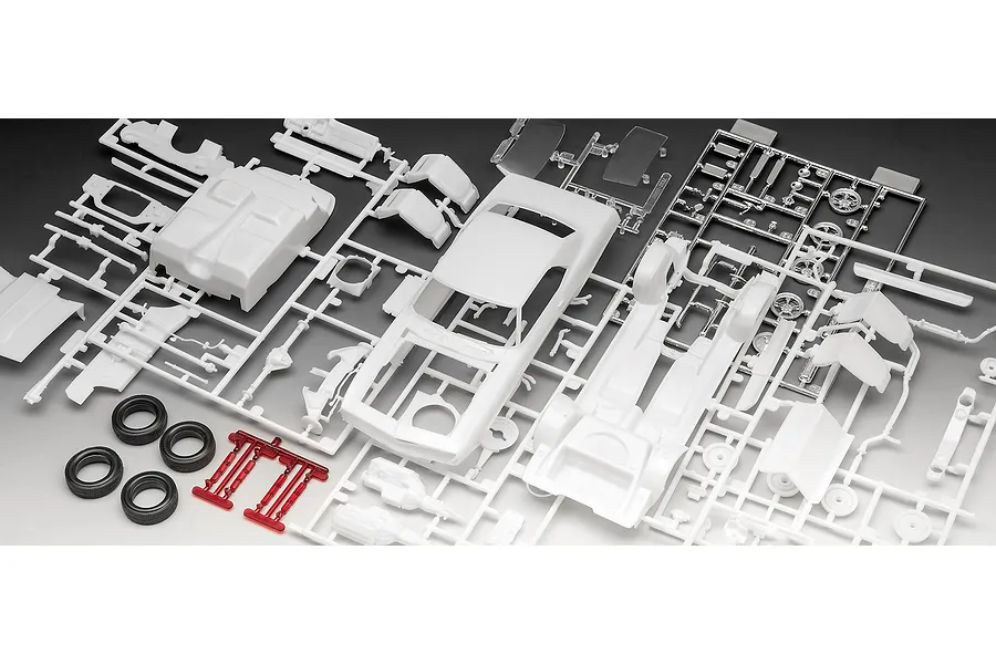 Unassembled plastic model kit parts for a 1969 Chevy Camaro, including white body shells, chrome-plated parts, and black rubber tires on a grey background.