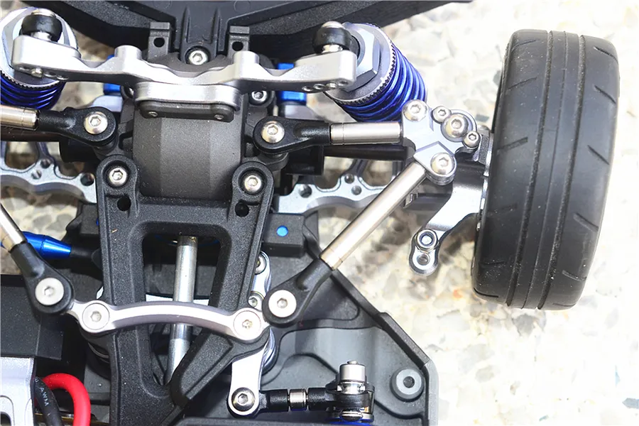 Close-up of the front suspension and steering assembly of an RC car featuring titanium tie rods and blue aluminium components.