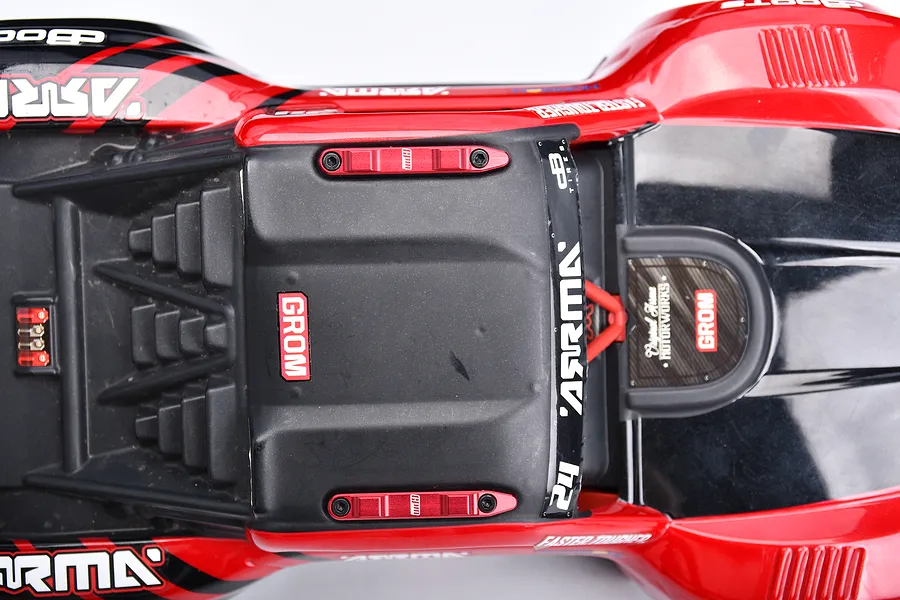 Top-down view of an Arrma Grom RC car body featuring red GPM Racing aluminium roof rails installed on the black roof section.