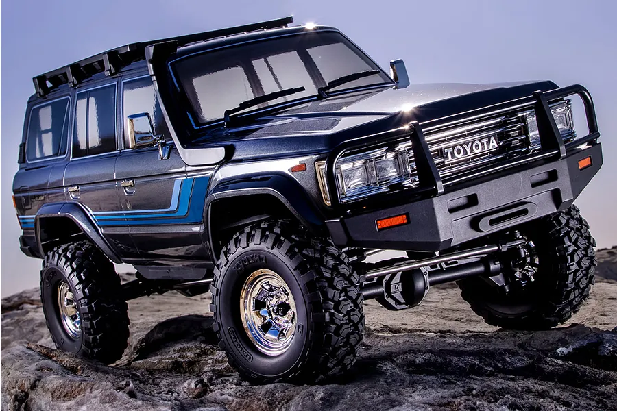 A blue Kyosho Toyota Land Cruiser 60 Series RC rock crawler parked on a rocky outdoor surface.