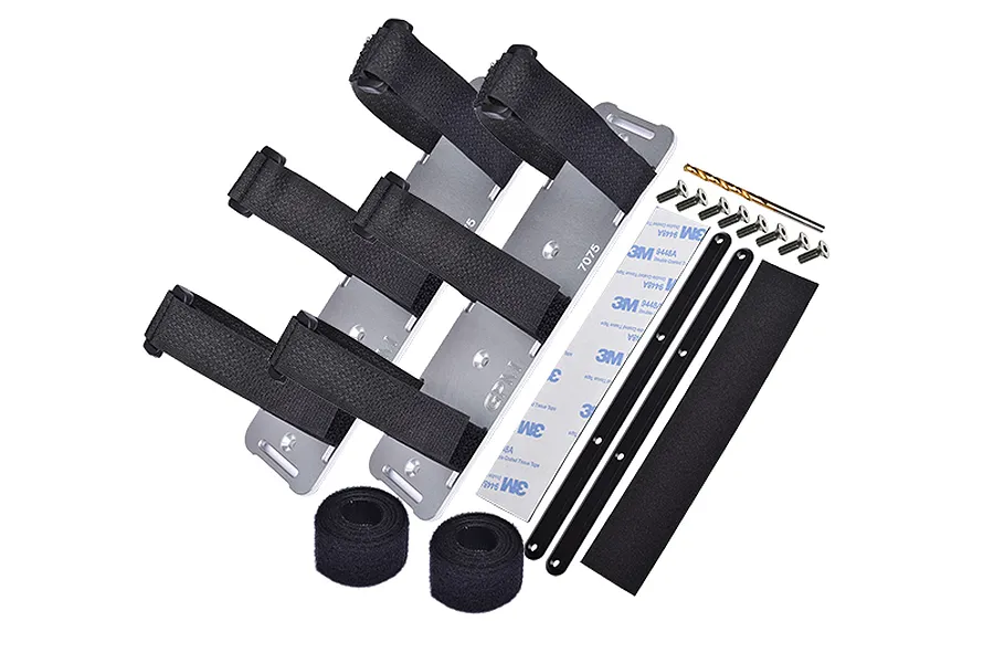 GPM Racing silver aluminium battery hold-down set for RC cars, including metal plates, velcro straps, screws, adhesive tape, and a drill bit.