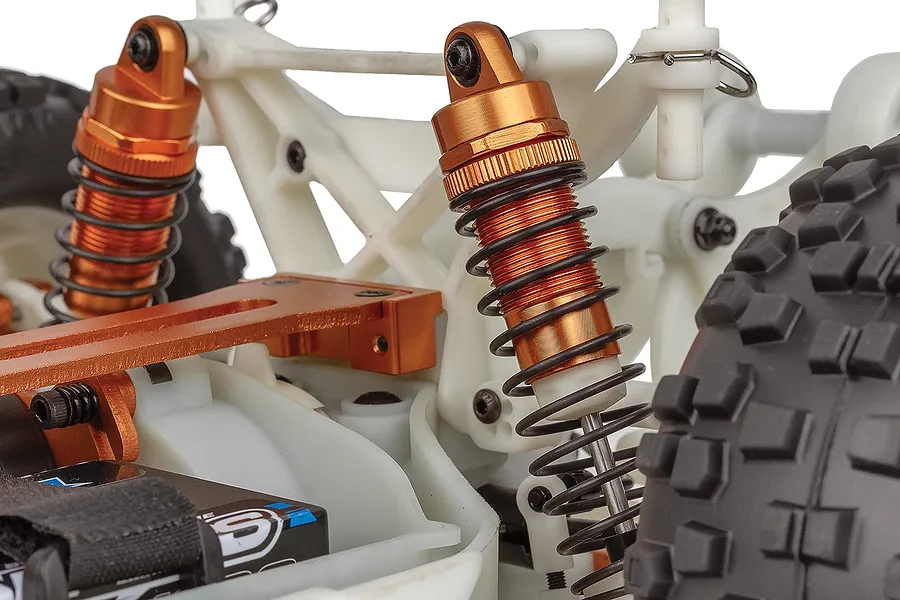 Close-up of the orange anodized shock absorbers and white plastic chassis components on a Team Associated Rival MT10 RC monster truck.