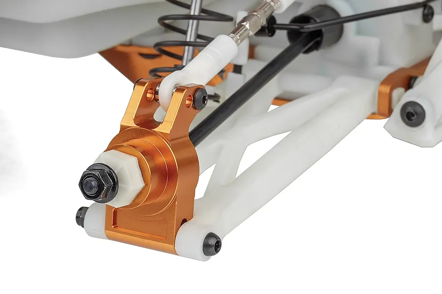 Close-up of the front suspension assembly on a Team Associated RC monster truck, featuring white plastic arms and orange anodized aluminum steering knuckles.