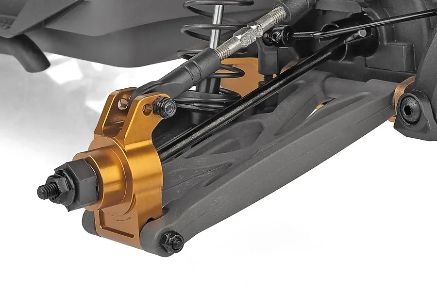 Close-up of the front suspension assembly on a Team Associated RC monster truck, featuring gold anodized aluminum steering knuckles and black plastic arms.