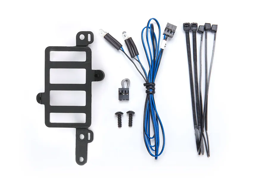 Traxxas Pro Scale lighting components including a black plastic mount, LED lights with wiring, zip ties, and small screws on a white background.