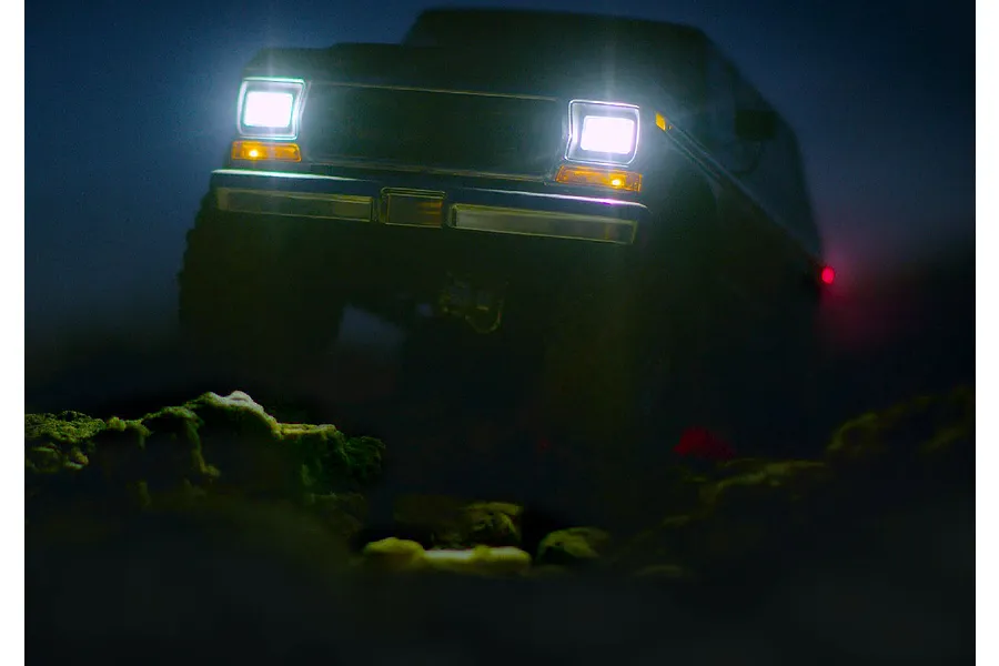 A dark, low-angle shot of an RC truck driving over rocks at night, with its bright LED headlights illuminated.