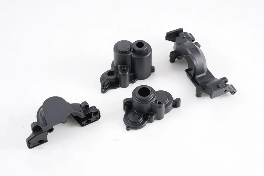 Four black plastic gearbox case components for an FMS RC vehicle arranged on a white background.