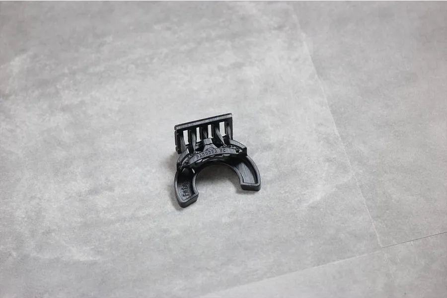 A black 3D printed RC transmitter steering wheel accessory by Pandora RC on a grey surface.